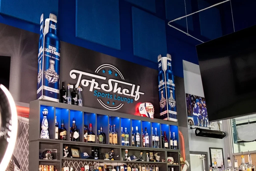 Top Shelf Sports Lounge bar with blue-lit liquor and hockey decor.