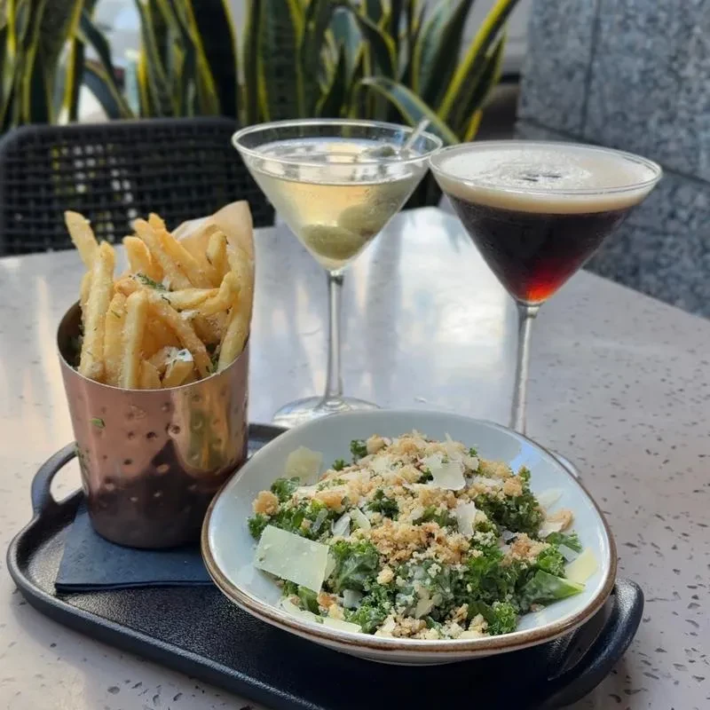French fries, salad, and two cocktails on a black serving tray.