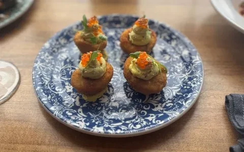 Four appetizers with golden base, creamy topping, orange fish roe, and herbs.