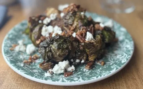 Roasted Brussels sprouts with crumbled cheese and pecans on a teal plate.