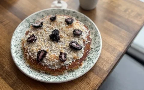 Pancakes topped with coconut and dark berries on a decorative plate.