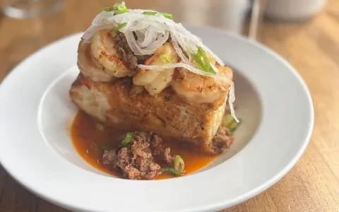Plated savory bread with shrimp, chorizo, sauce, and green onions.