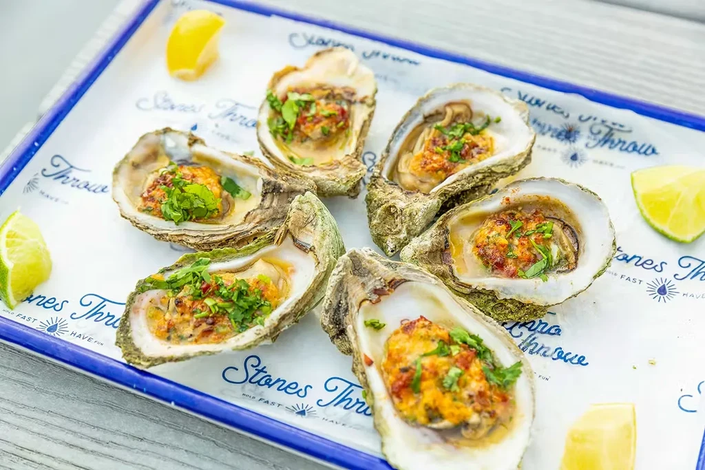 Six baked oysters with herb gratin, lemon, and lime on a tray.