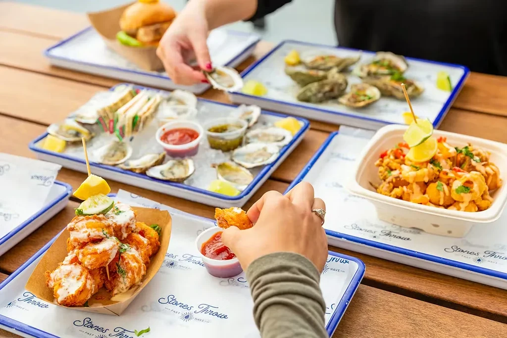 Various appetizers including oysters, sandwiches, and fried bites on a wooden table.