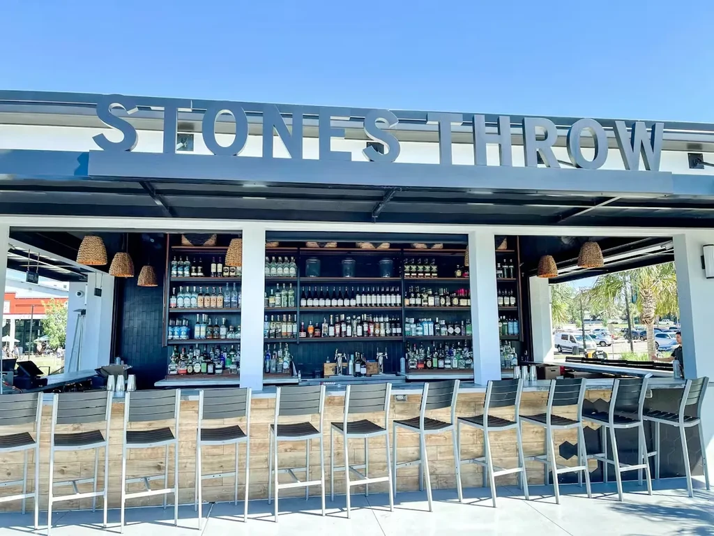 Exterior of "STONES THROW" bar with modern stools and stocked back bar.