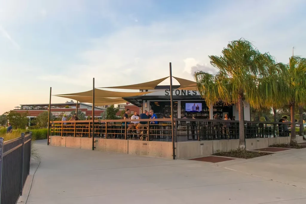 People socialize on 'STONES' outdoor bar patio under shade sails.