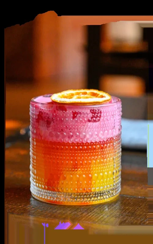 Vibrant gradient cocktail in textured glass, garnished with fruit and orange slice.