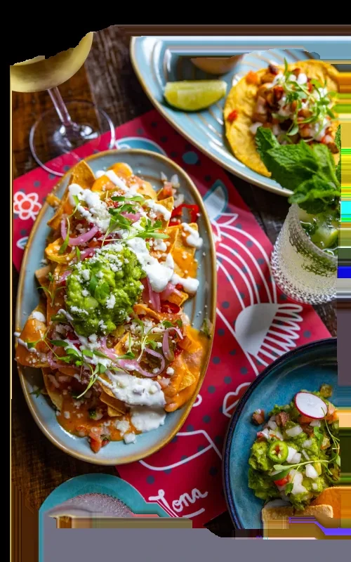 Top-down: Nachos, taco, guacamole, and a drink on rustic wooden table.