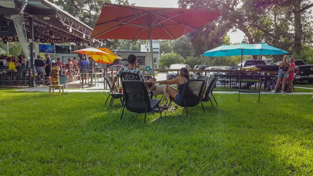 Outdoor restaurant patio with diners, bar, umbrellas, lawn, and a dog.