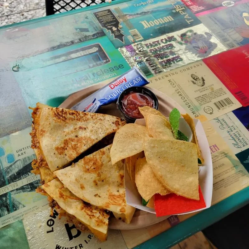 Overhead shot: Quesadilla, chips, salsa, sour cream on a label-covered table.