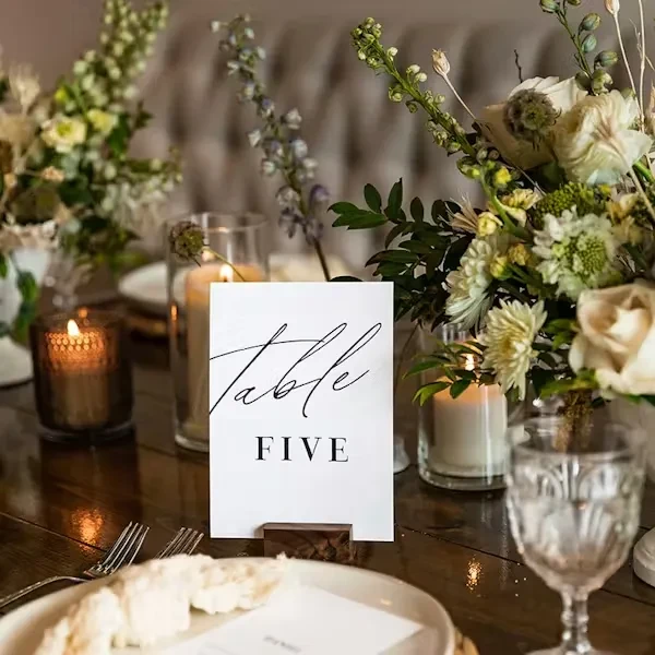 Dining table with 'Table FIVE' card, white flowers, and glowing candles.