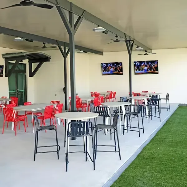 Modern, empty restaurant patio with red chairs, dark stools, and TVs.