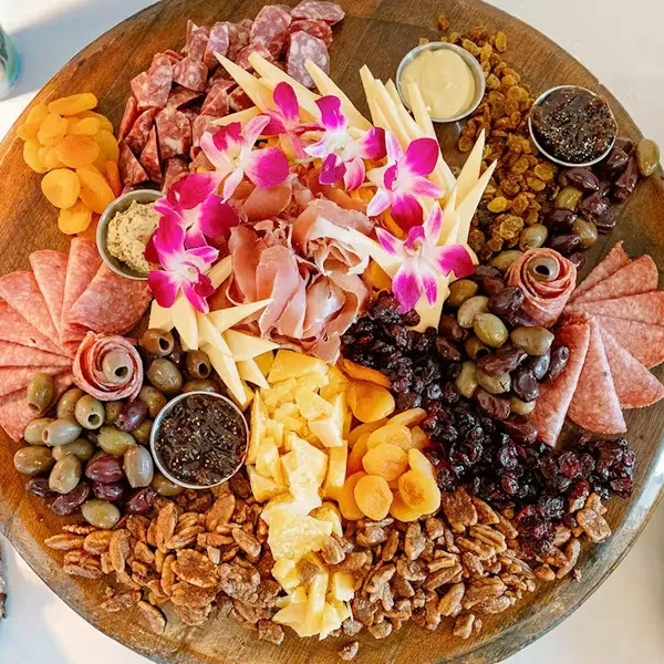 Vibrant charcuterie board with meats, cheeses, fruits, nuts, and orchid garnish.