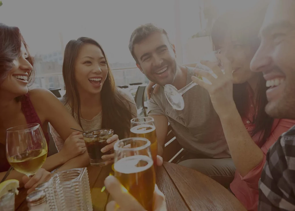 Group of young adults laughing and drinking at a table.
