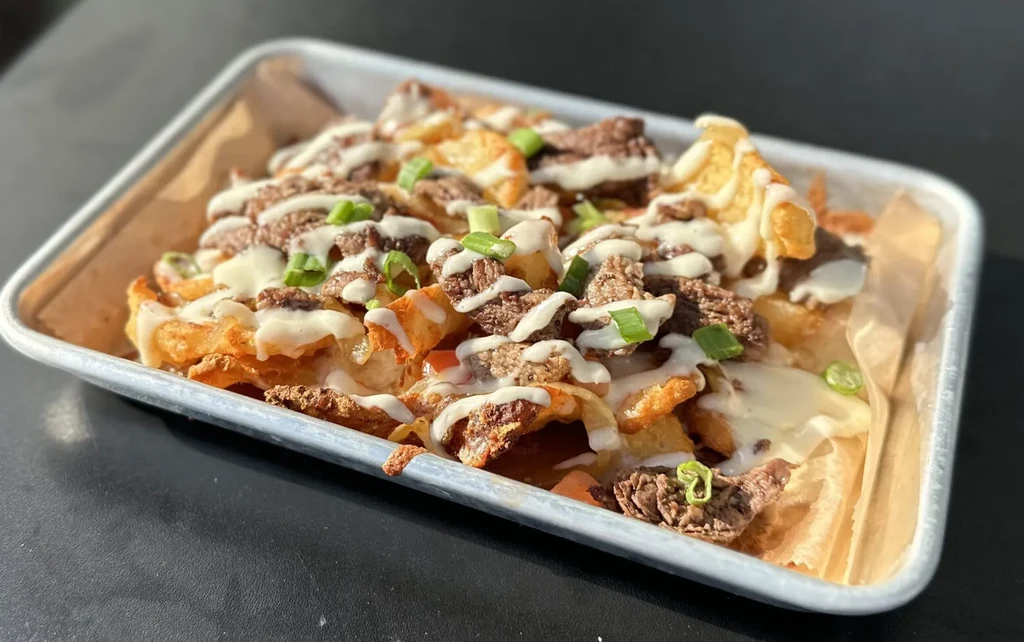 Close-up: Loaded fries in tray, topped with beef, cheese, green onions.