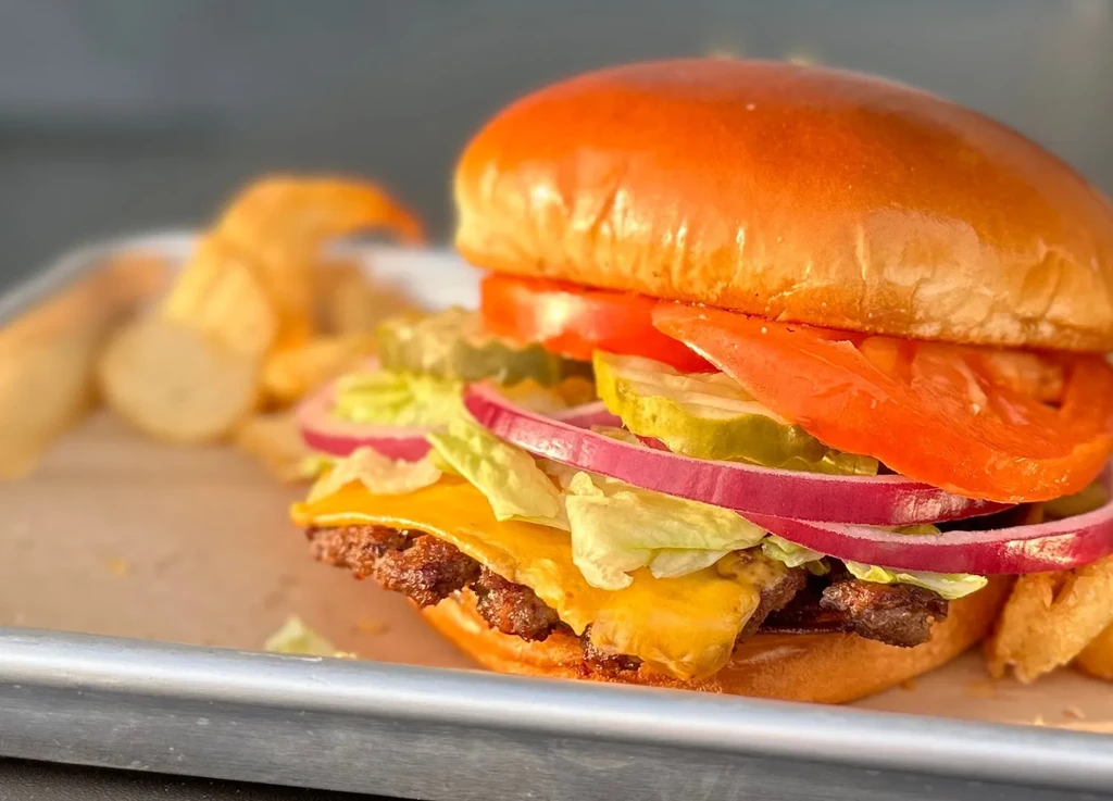 Close-up of a stacked burger with double patties, cheese, and vegetables.