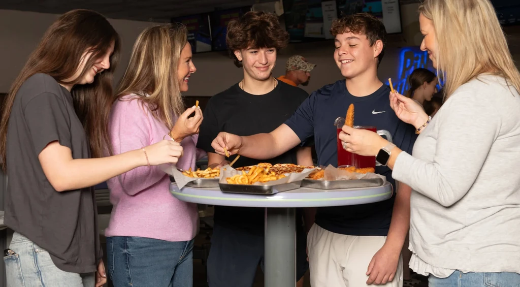 Five people share fries, pizza, and drinks at a high-top table.