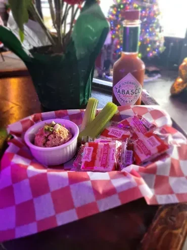 Serving basket with dip, celery, crackers, Tabasco, under purple light.