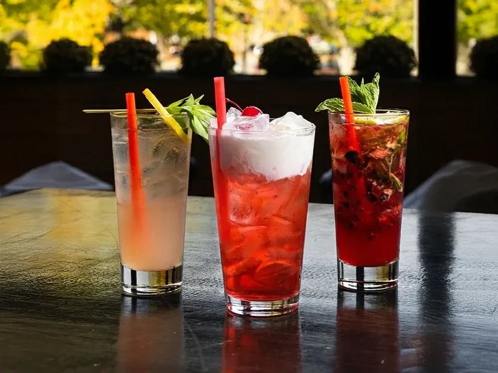 Three colorful garnished cocktails, pink, red, and purple, with ice.