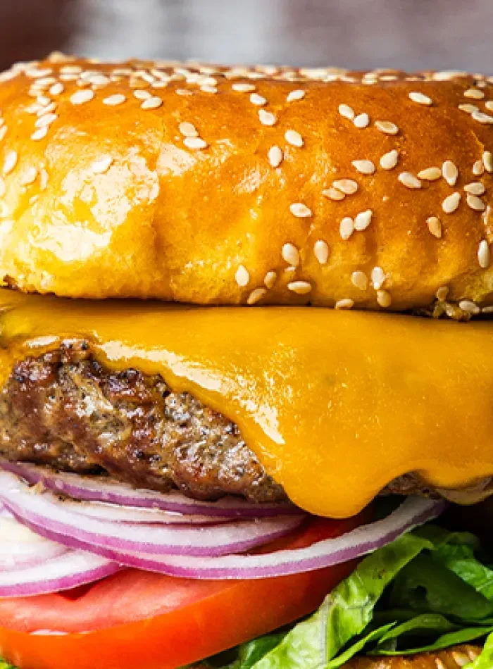 A burger with bun, melted cheese, beef patty, onion, tomato, and lettuce.