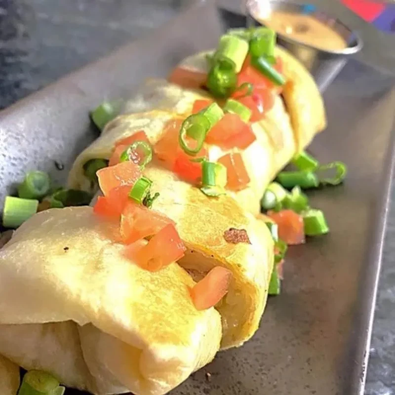 Three savory rolls topped with tomatoes, green onions, and dipping sauce.