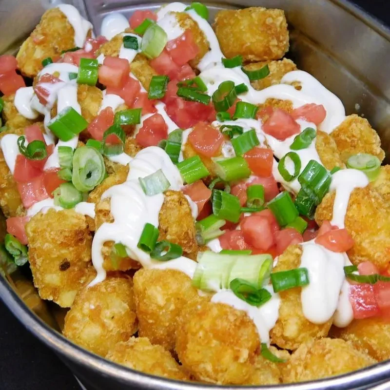 Tater tots with creamy sauce, red tomatoes, and green scallions.