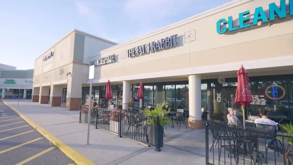 Modern strip mall with 'THE FAT RABBIT' restaurant patio on a sunny day.
