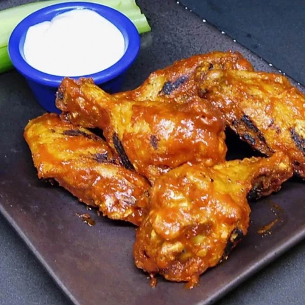 Charred buffalo chicken wings, white dipping sauce, and celery on plate.