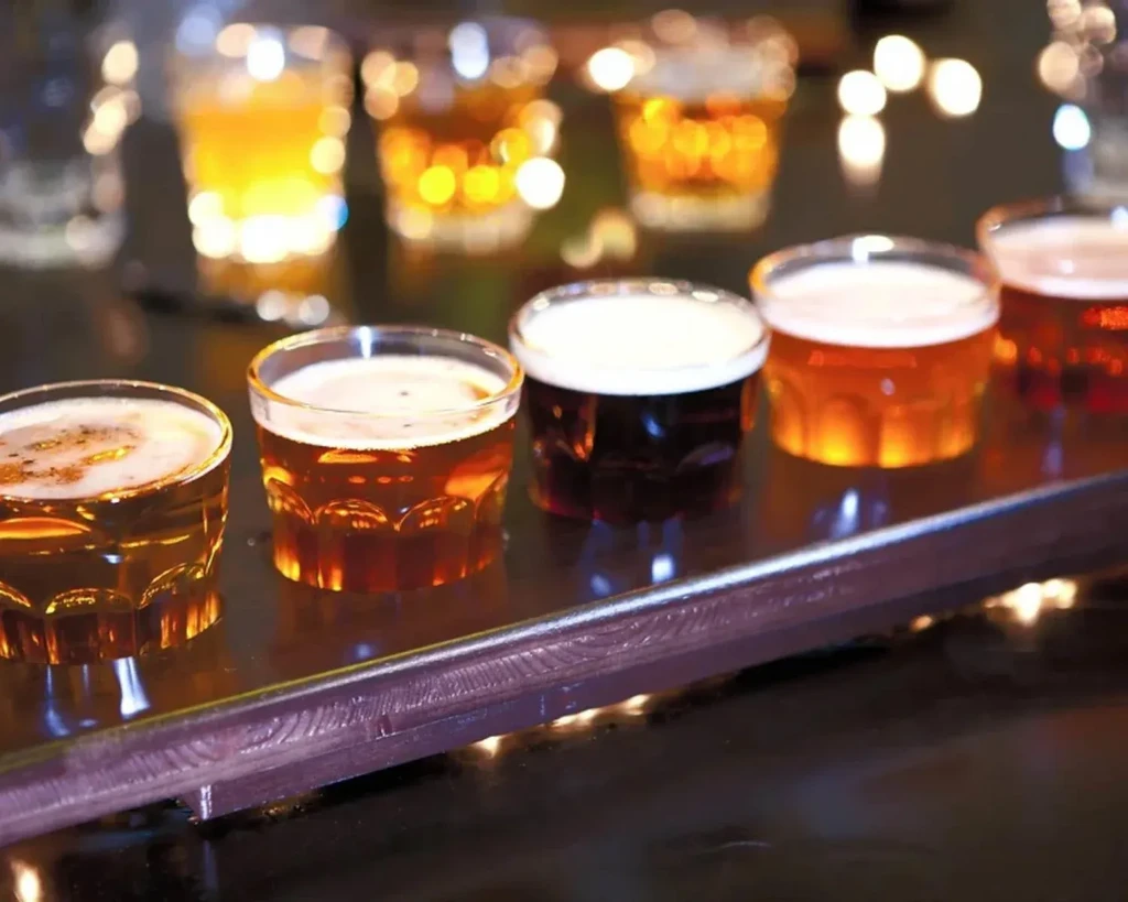 Five distinct beers in a flight on a dark, reflective bar.