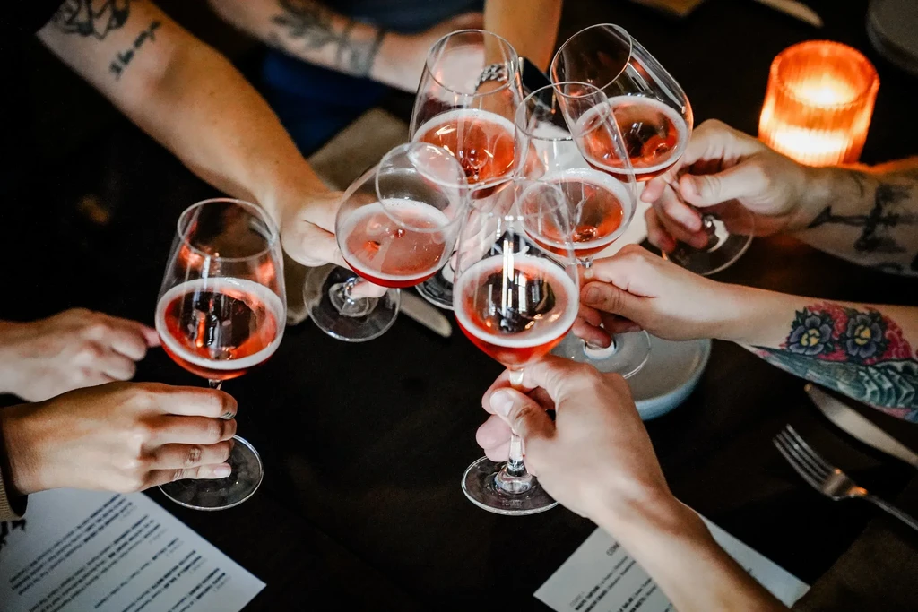 Seven hands clinking rosé wine glasses; some arms show tattoos.