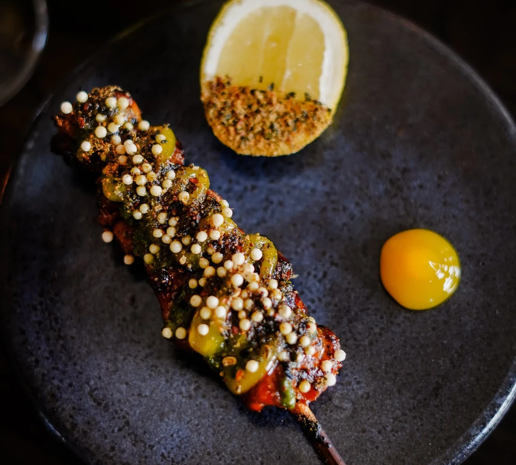 Skewer with green sauce, white spheres, lemon, and yellow puree.