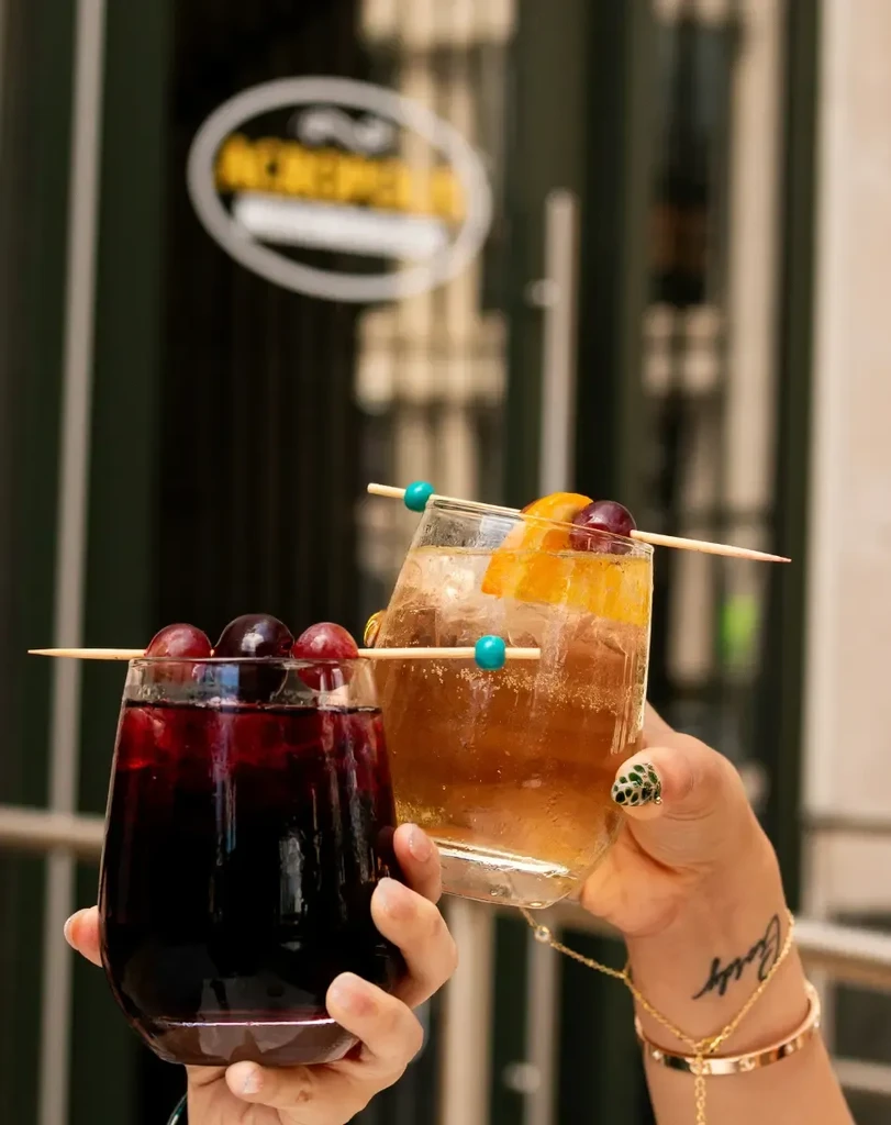 Two hands hold a red drink and an amber drink with fruit.
