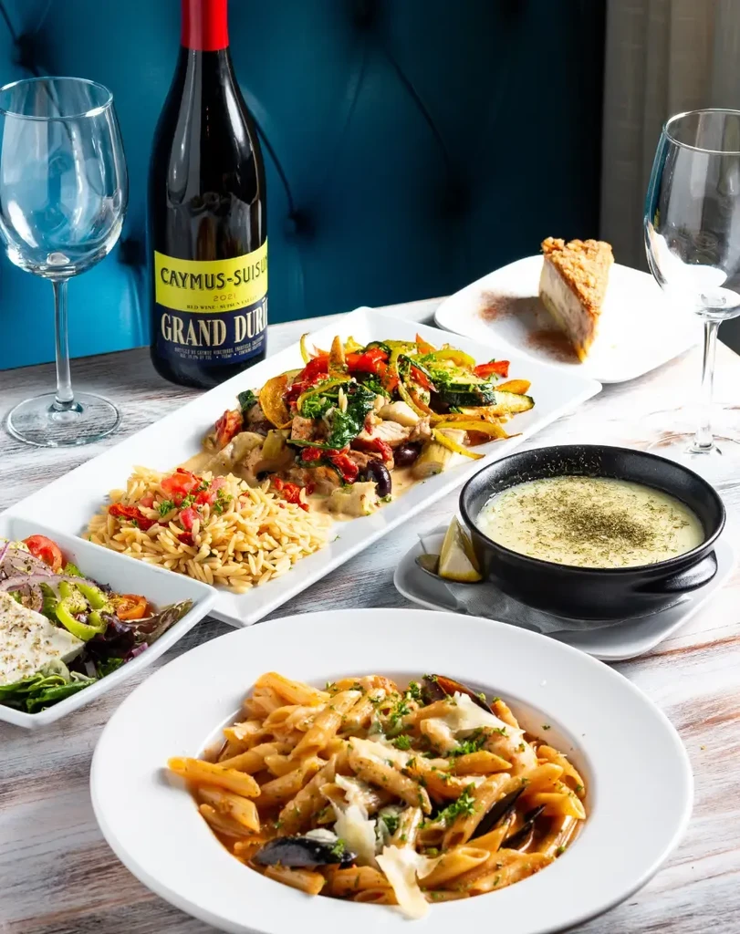 Restaurant table with pasta, salad, soup, wine, and dessert.