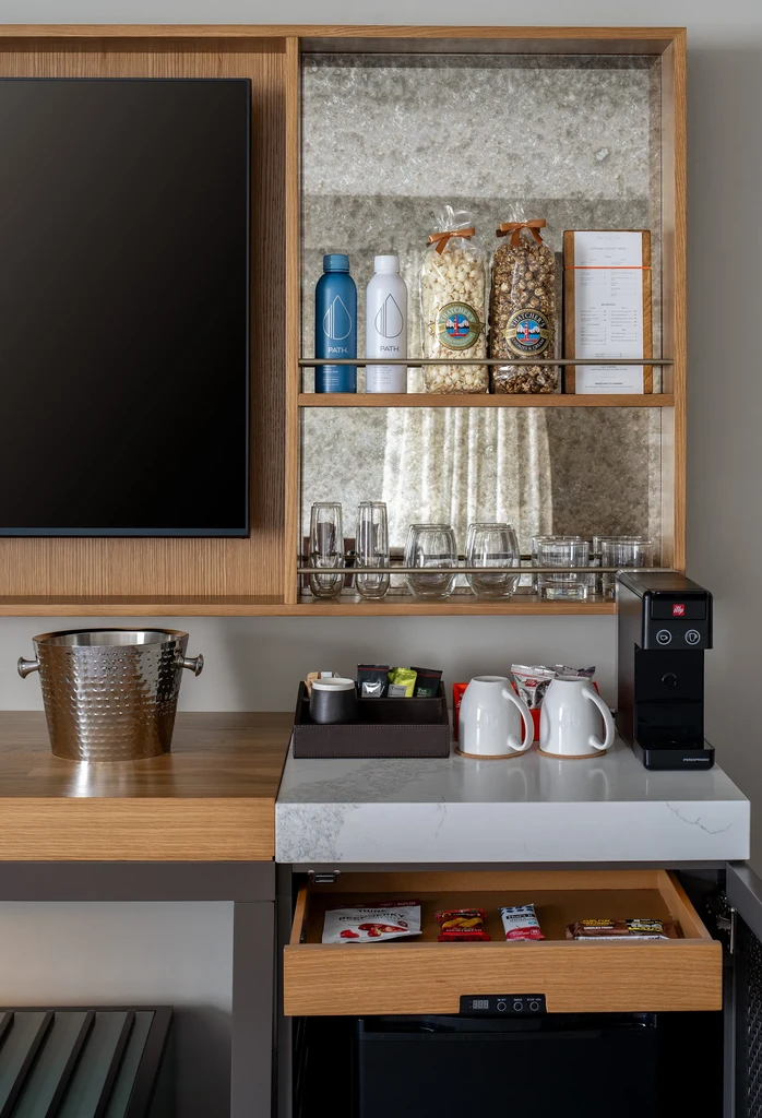 Modern refreshment station with coffee, snacks, drinks, glassware, and mini-fridge.