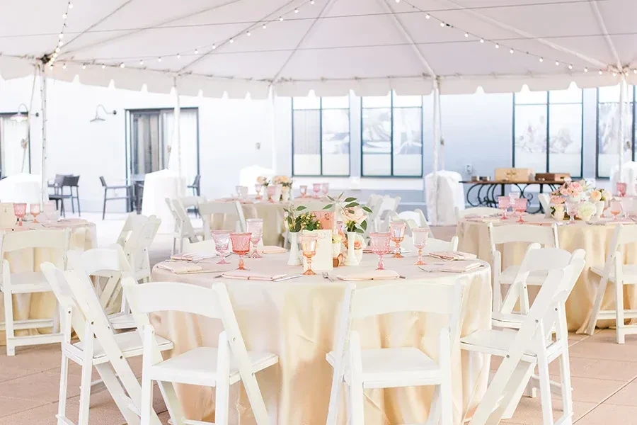 Elegant tent setup with tables, pink goblets, flowers, and lights.