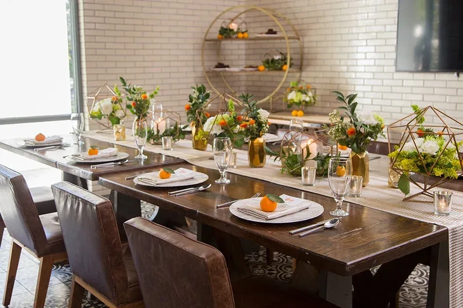 Elaborately set long dining table with floral centerpieces and oranges.