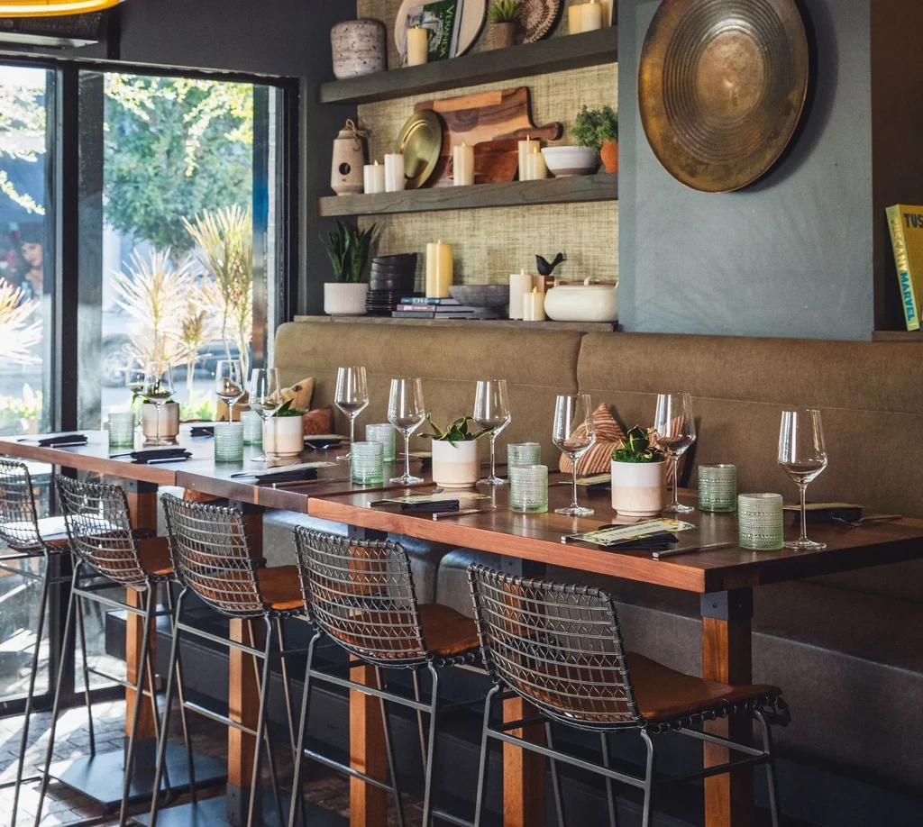 Long high-top communal table and banquette in a bright restaurant.