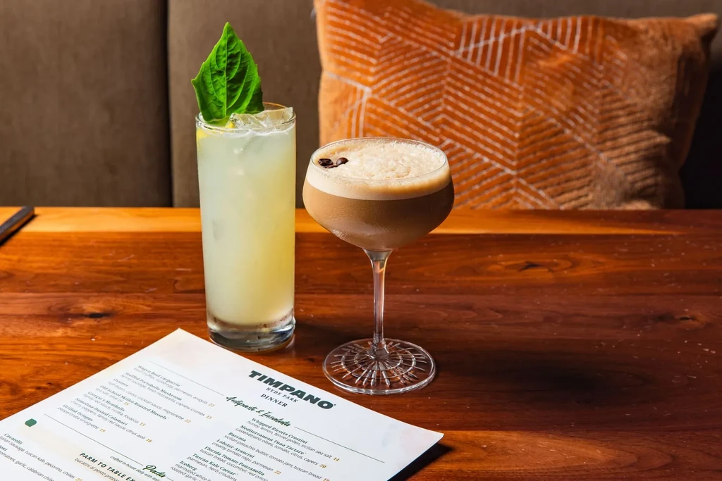 Two cocktails and a 'TIMPANO HYDE PARK' dinner menu on a table.