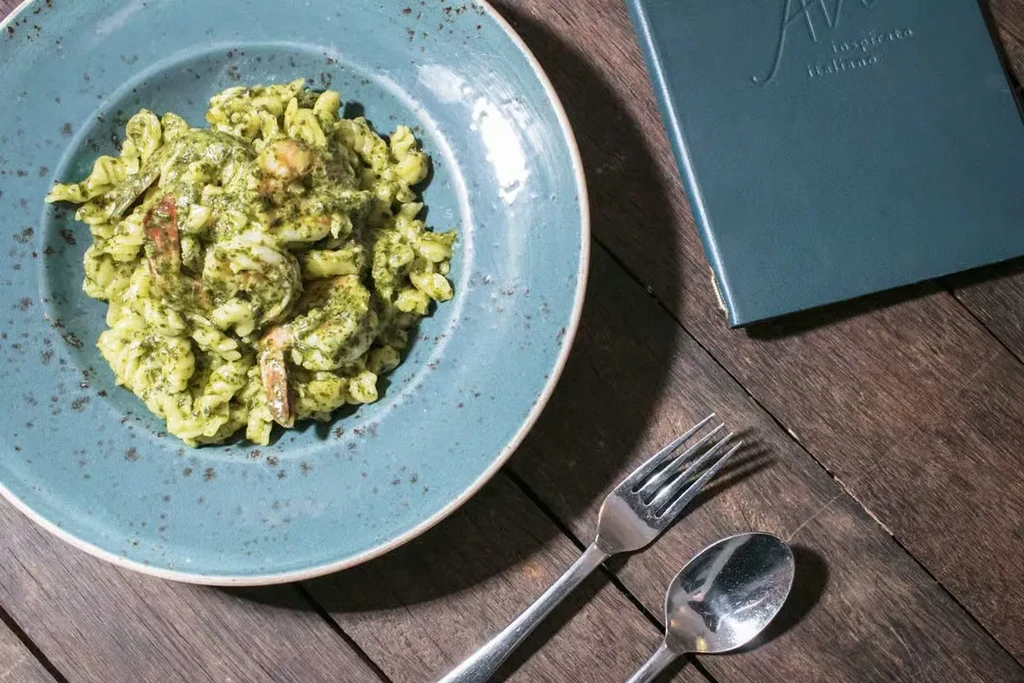 Pesto shrimp pasta plate with 'AVO' menu on a wooden table.