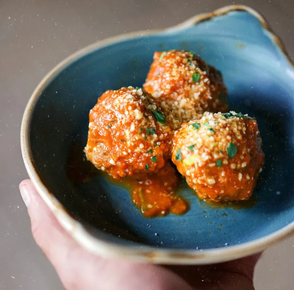 Meatballs in orange-red sauce, topped with Parmesan and herbs, teal bowl.
