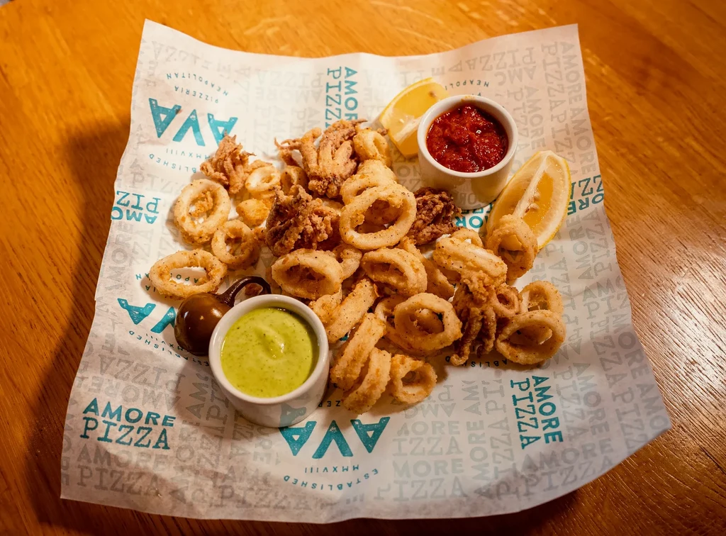 Crispy golden fried calamari, sauces, and lemon on branded paper.
