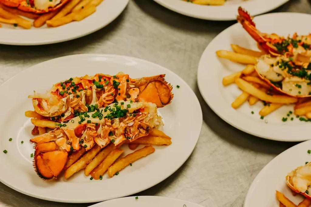 Several plates of lobster tail, chives, and french fries.