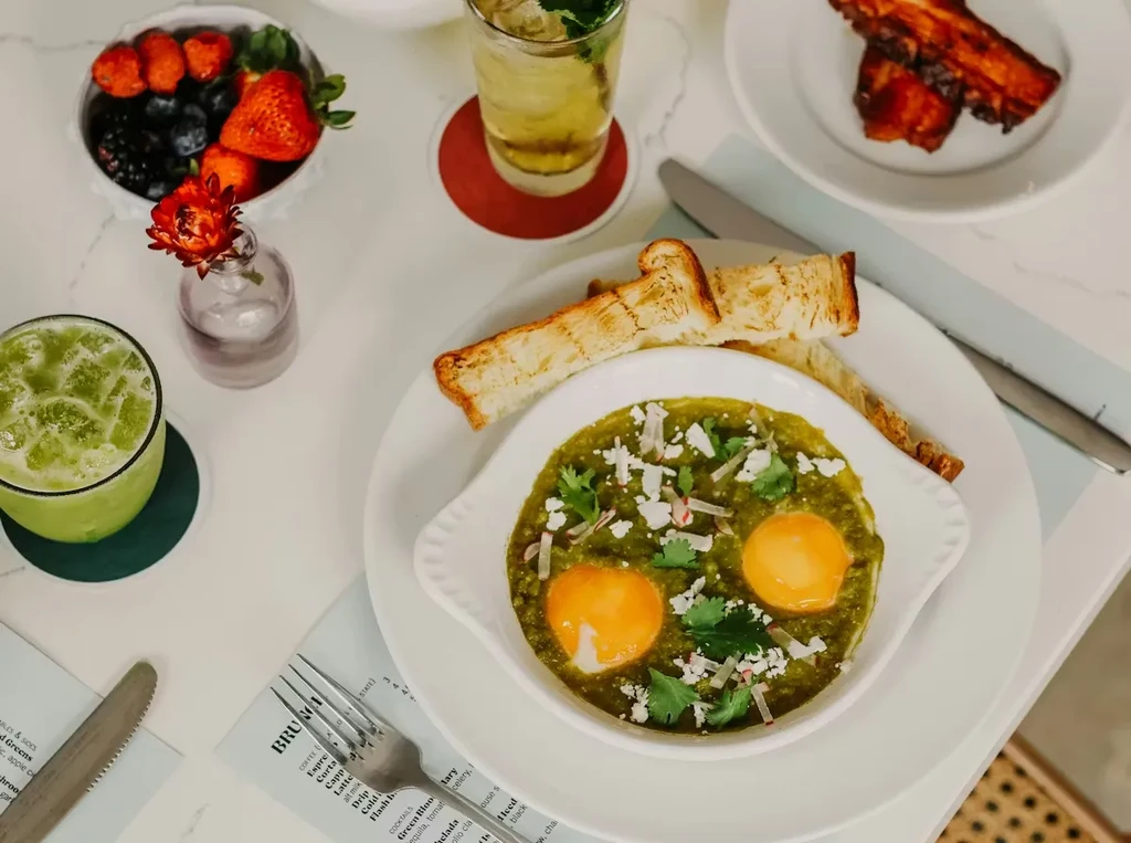 Brunch table with eggs in salsa verde, toast, berries, and drinks.
