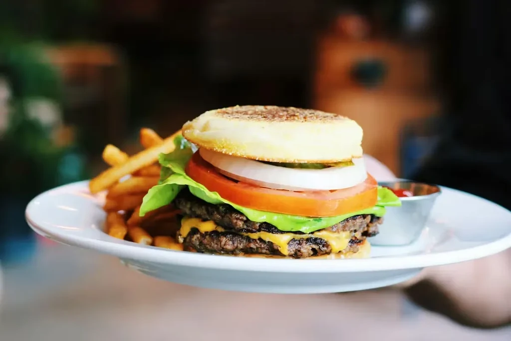 Hand holding plate with double cheeseburger, french fries, and ketchup.