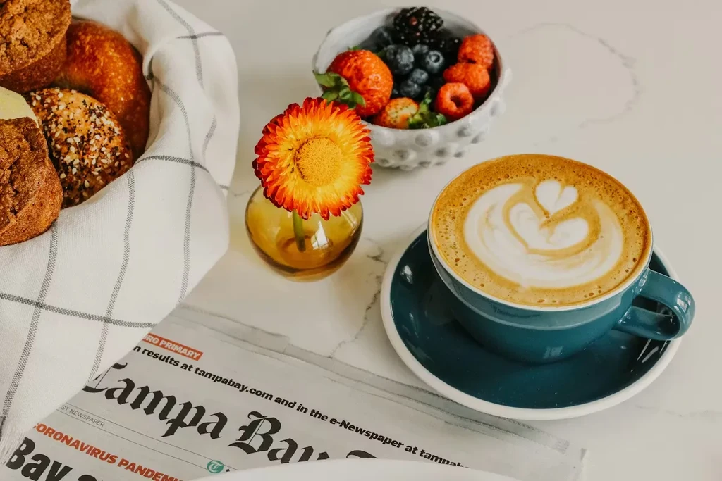 Breakfast scene featuring latte, berries, baked goods, and a newspaper.