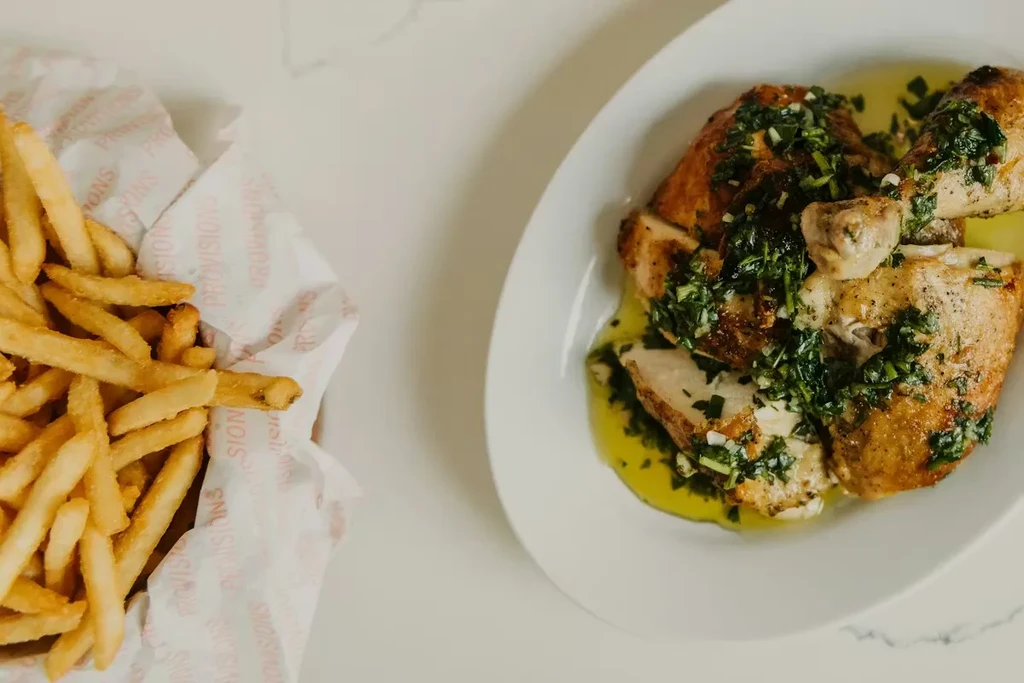 Roasted chicken with bright green sauce alongside golden-brown french fries.