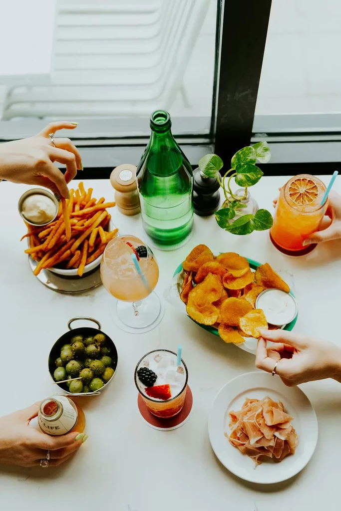 Overhead view of table with appetizers, cocktails, and hands reaching.