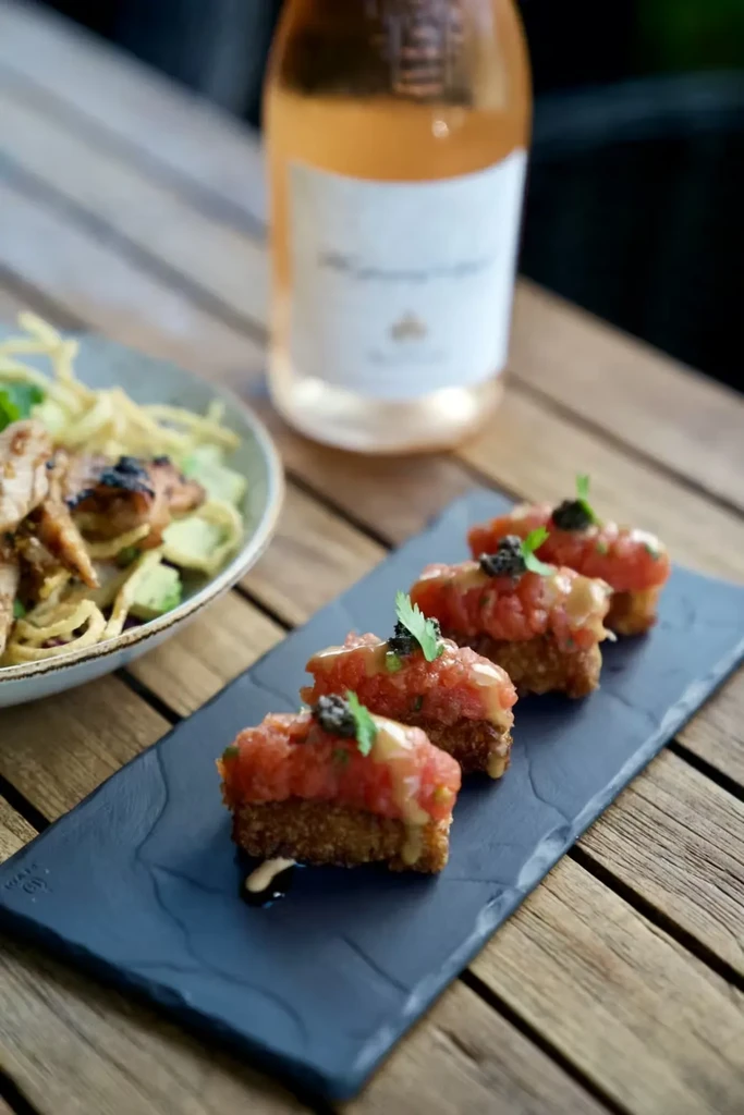 Tuna tartare with caviar, chicken salad, and rosé wine on wooden table.