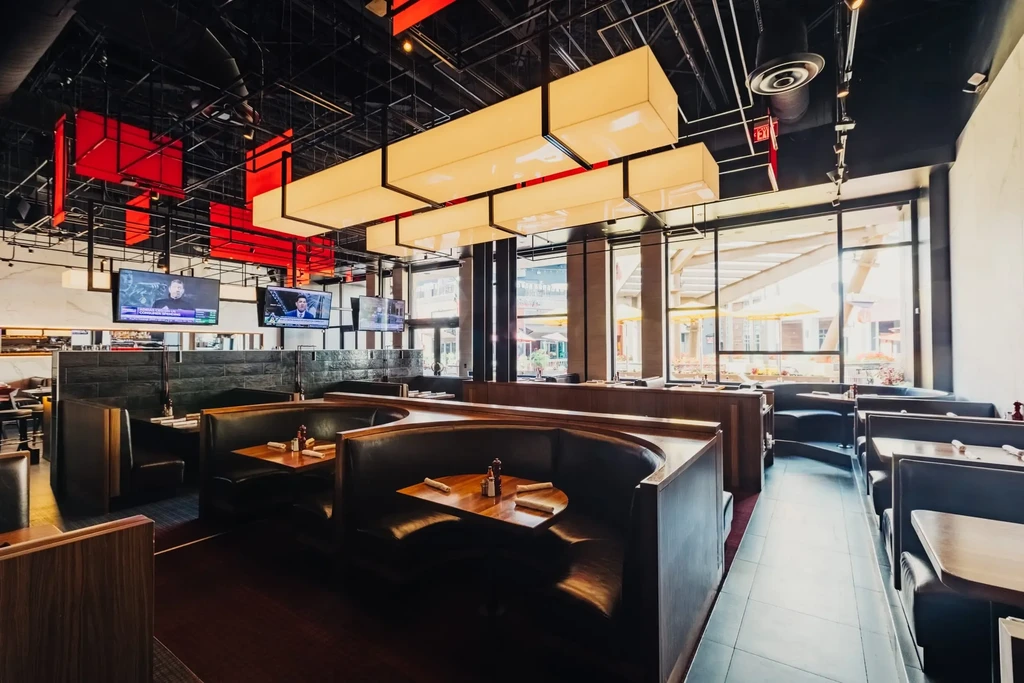 Modern restaurant interior: dark leather booths, exposed ceiling, TVs, outdoor view.