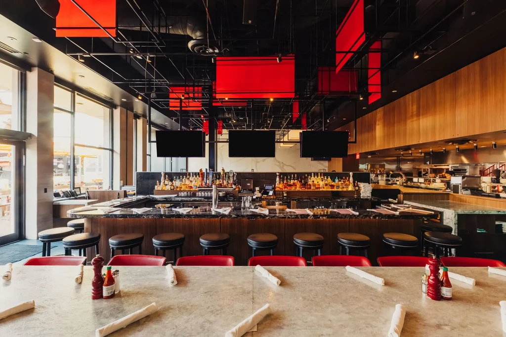 Industrial-chic restaurant with red chairs, well-stocked bar, open kitchen.